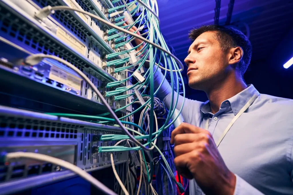 Technik kontroluje síťové kabely připojené k serverům v jasně osvětleném datovém centru.