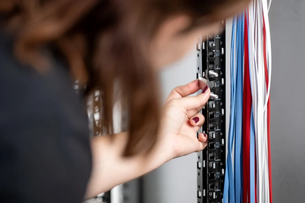 Close-up of a technician fitting a PATCHBOX /dev/mount onto a rack rail beside blue, red and white cables.
