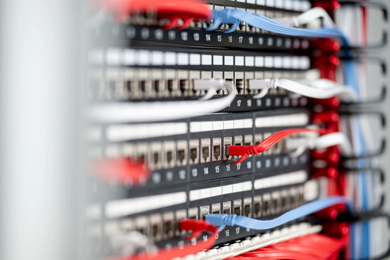 Close-up of patch panels in a network rack with numbered ports and red, blue, and white network cables.